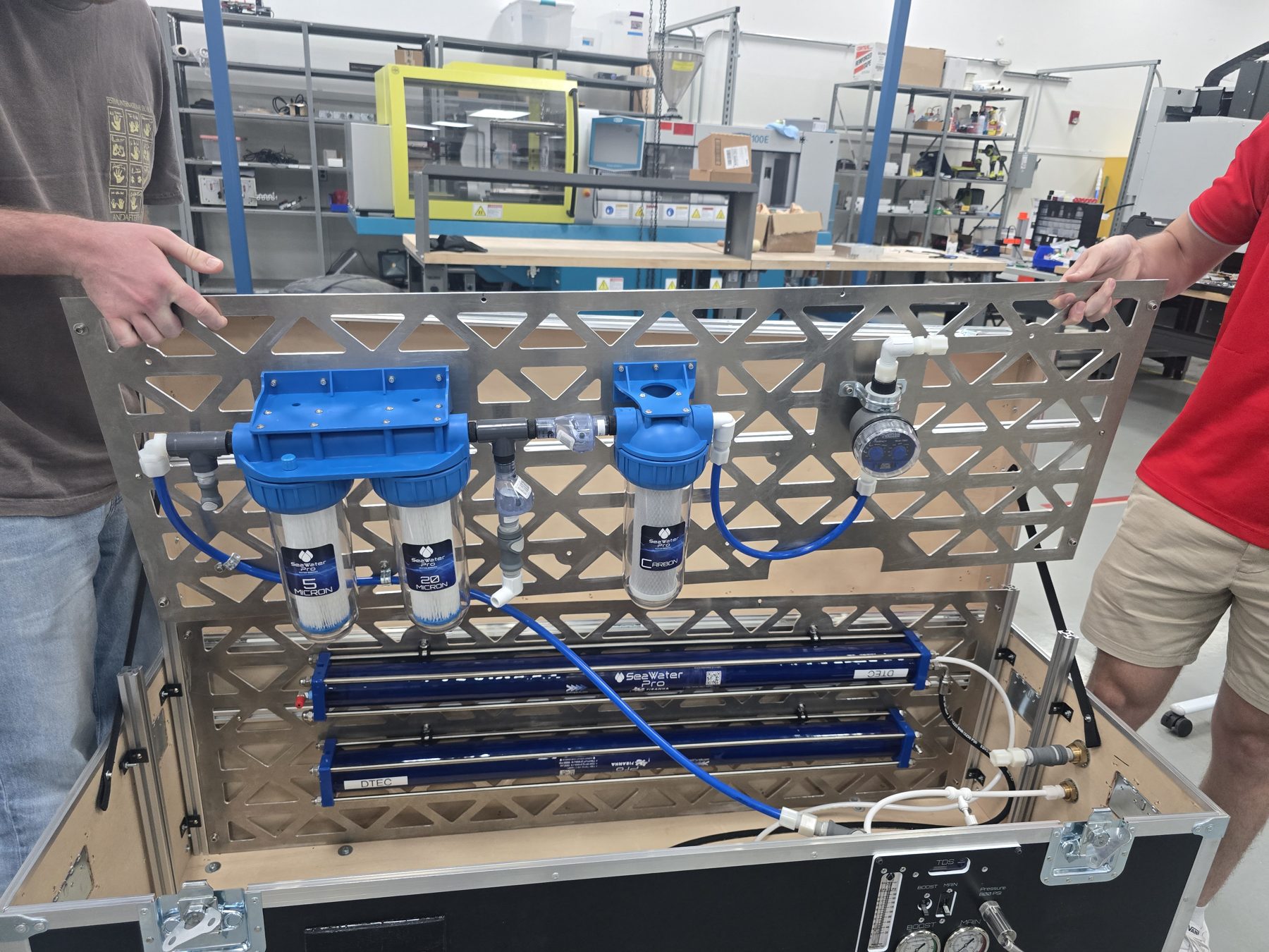 Engineers holding a ruggedized, case-mounted water treatment system built by Plitzie