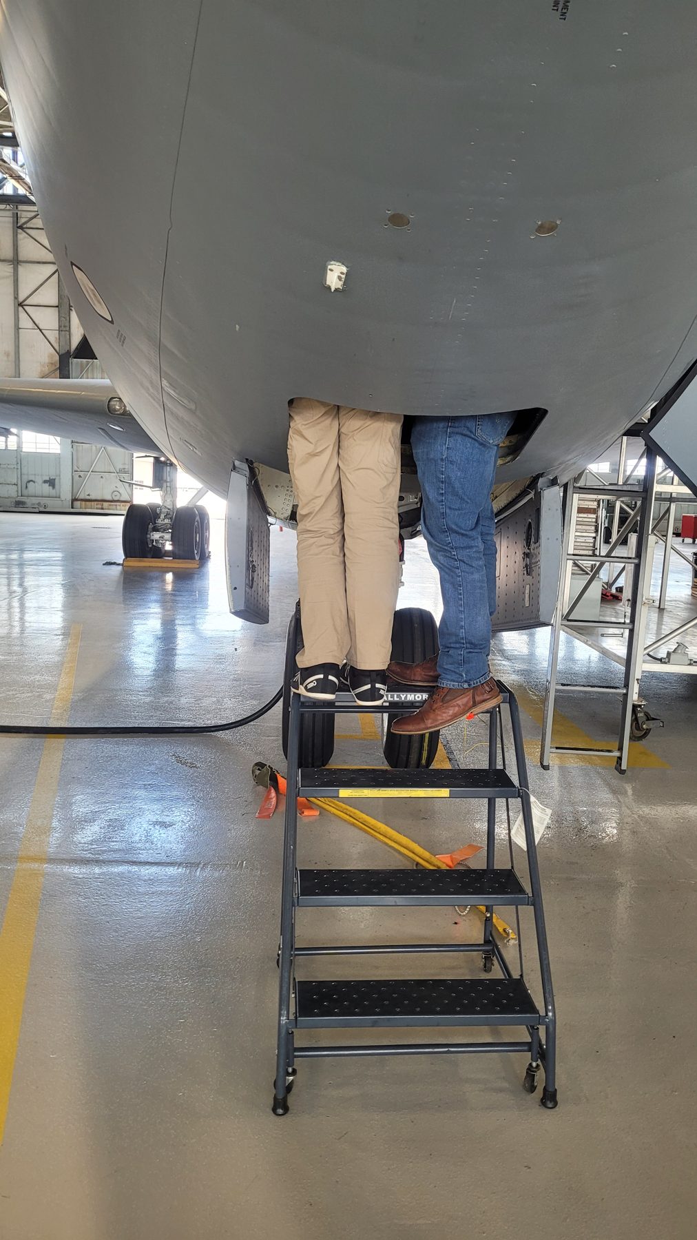 Two Plitzie engineers on a work stand with their upper bodies inside an aircraft's underside access bay